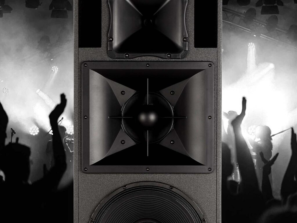 Een foto van de RCF NX 985-A luidspreker zonder beschermingsrooster. Op de achtergrond is een concert of optreden zichtbaar gezien vanuit het publiek. De foto is in greyscale.