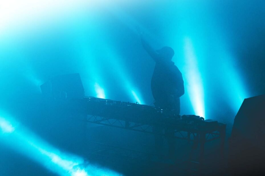 Een foto van een DJ op een podium tussen de blauw uitgelichte rook.