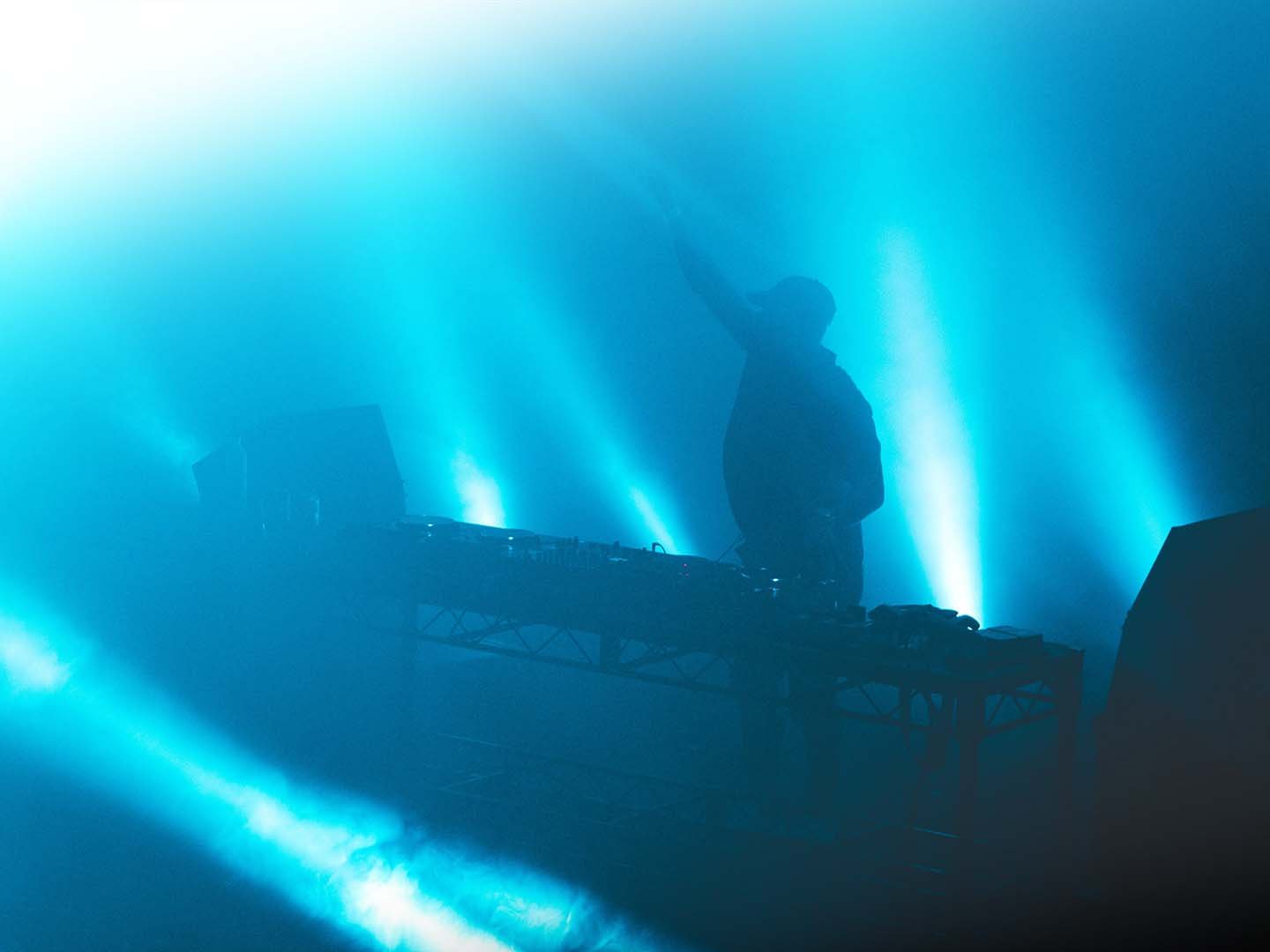 Een foto van een DJ op een podium tussen de blauw uitgelichte rook.